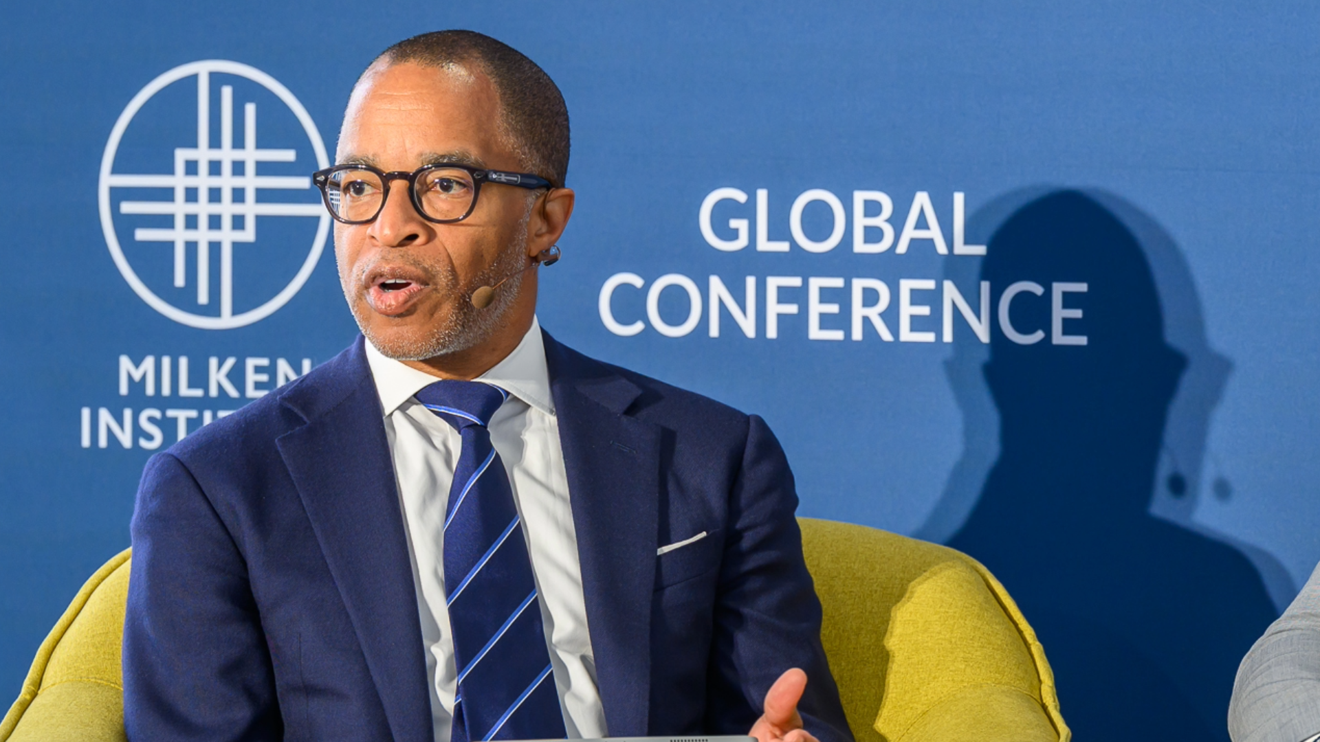 Professional man in navy suit and glasses at Global Conference with blue backdrop