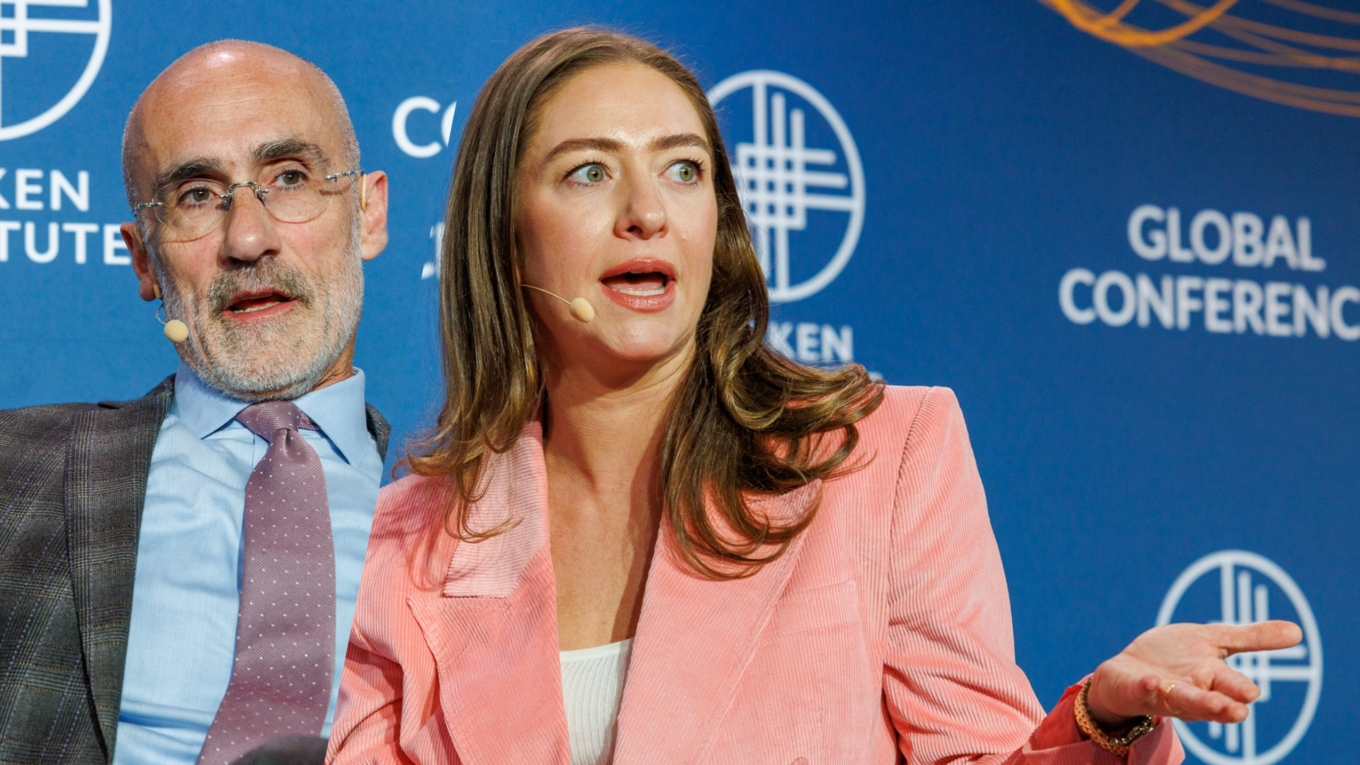 Woman in pink blazer speaking at Global Conference podium with man standing behind her