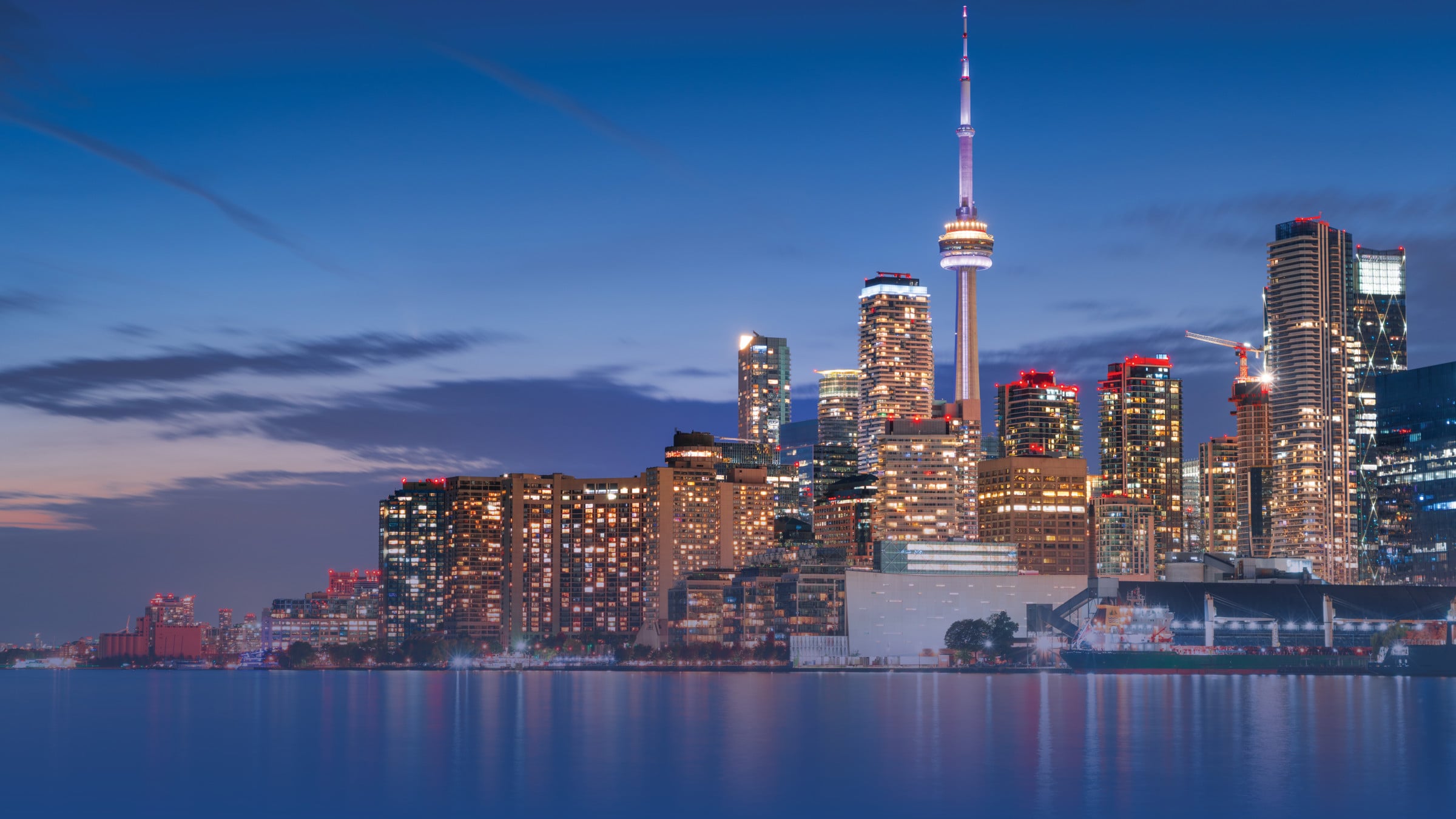 Toronto skyline at dusk with CN Tower and illuminated buildings reflected in Lake Ontario