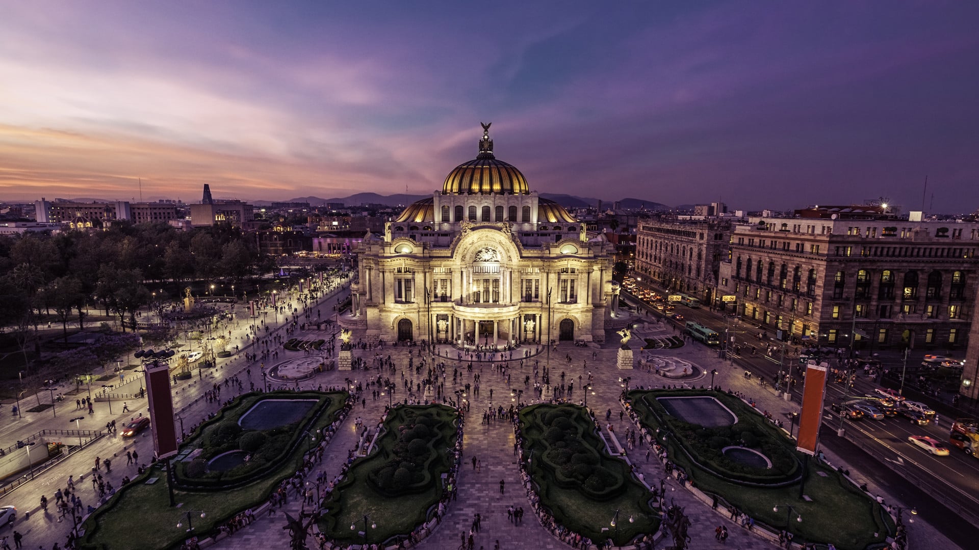 Grand white cathedral with golden domes illuminated at dusk in city plaza with purple sky