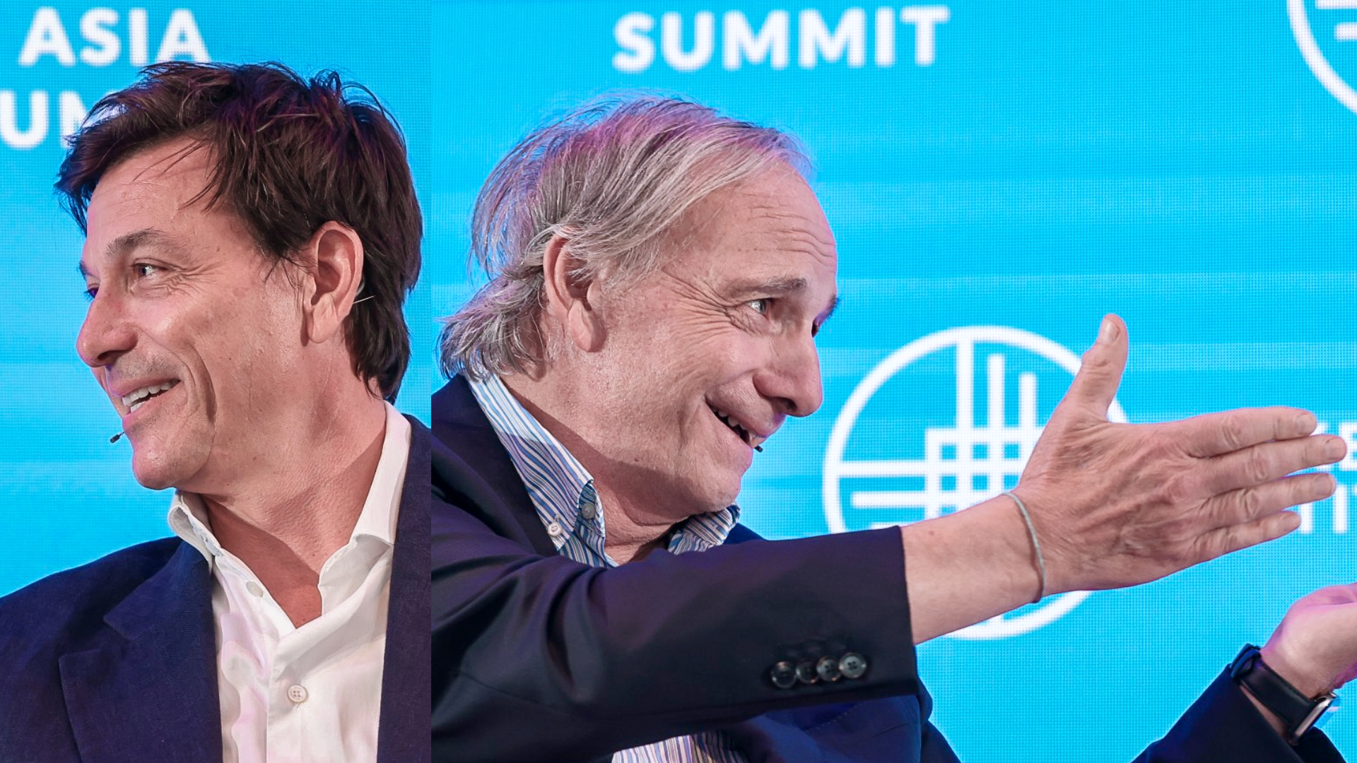 Two businessmen in suits gesturing at a summit event with blue backdrop
