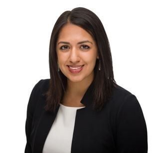 A smiling dark-skinned female-presenting person with dark hair wearing a white shirt and dark suit jacket against a white background.