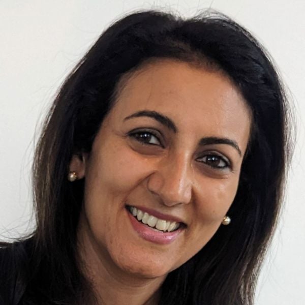 Smiling medium-skinned, female-presenting individual with medium length dark hair wearing a black shirt