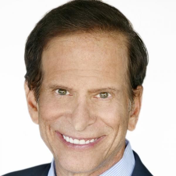 A smiling light-skinned male-presenting person with short, brown hair wearing a suit against a white background