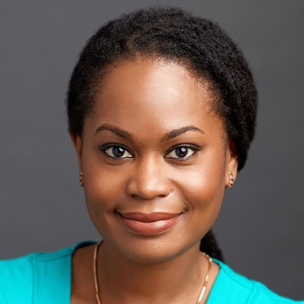 A smiling darker-skinned female-presenting person with black hair wearing a turquoise shirt against a gray gradient background