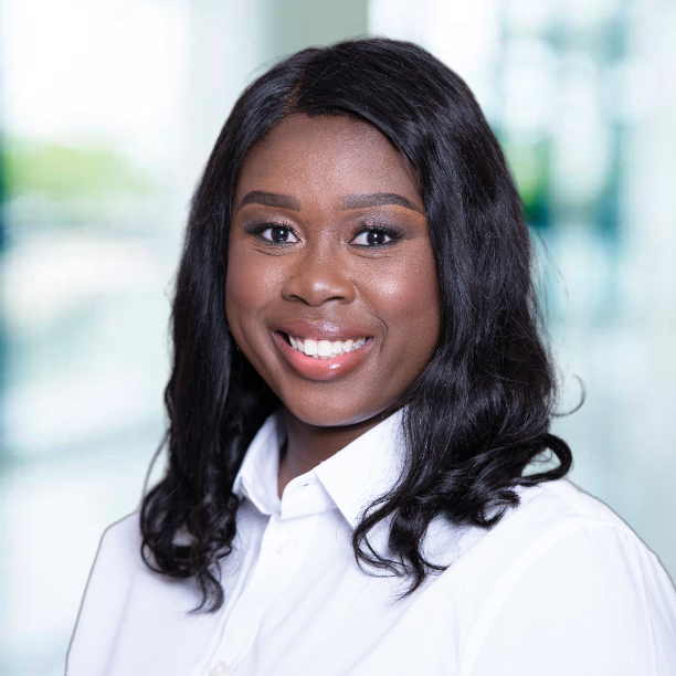A smiling female-presenting dark-skinned individual with dark hair wearing a white shirt against a blurred background