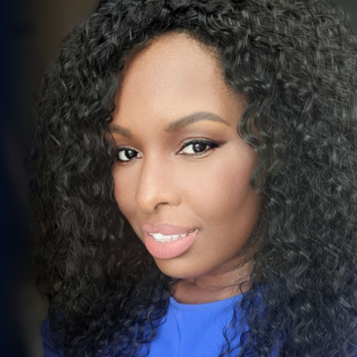 Smiling dark-skinned, female-presenting individual with long dark hair wearing a blue shirt on a dark backdrop.