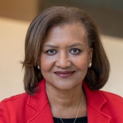 A smiling darker-skinnned female with short brown hair wearing a red jacket against an ambiguous background