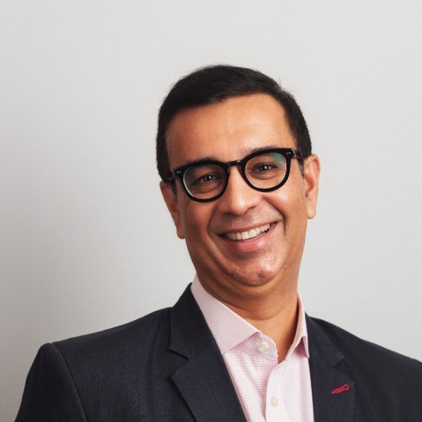 Smiling light-skinned, male-presenting individual with short dark hair wearing a dark suit on a grey backdrop.