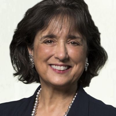 Smiling light-skinned, female-presenting individual with short dark hair wearing a black shirt on a light backdrop.