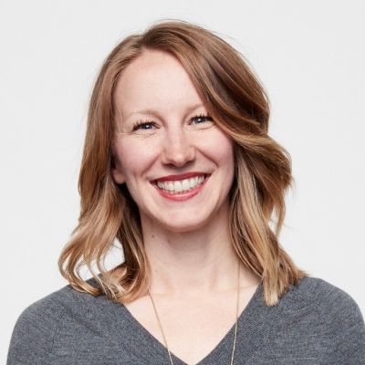 A smiling light-skinned female with light brown hair wearing a gray shirt against a white background