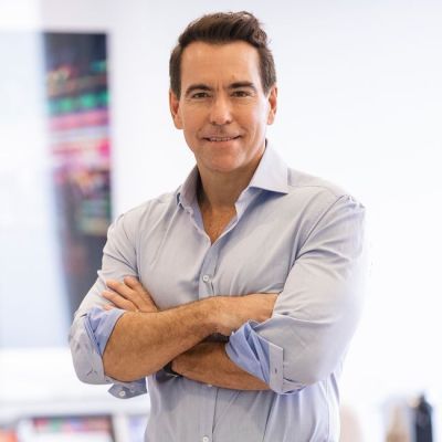 Smiling light-skinned, male-presenting individual with short dark hair wearing a grey shirt with arms folded