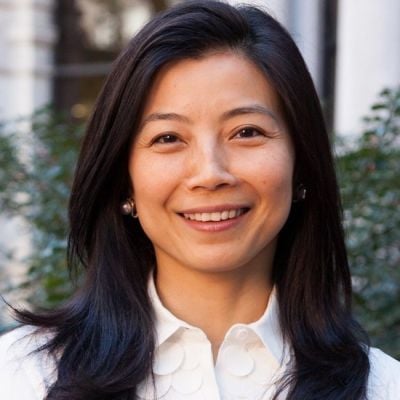 A smiling female-presenting person of Asian heritage with black hair wearing a white shirt against an outdoor setting