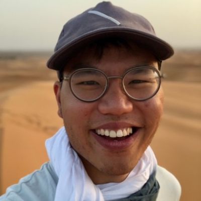 Smiling male-presenting individual wearing a hat, white scarf outdoors