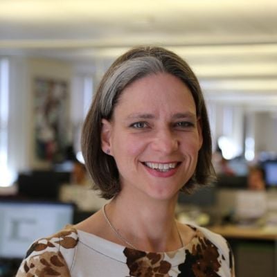 A smiling light-skinned female with short brown and gray hair wearing a patterned shirt against an ambiguous background