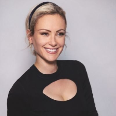 A smiling light-skinned female with blonde hair wearing a black shirt against a light gray background