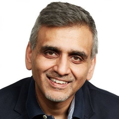 A smiling male-presenting person with gray hair wearing a dark shirt against a white background