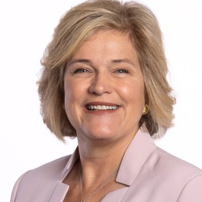 A smiling light-skinned female with short blonde hair wearing a blush pink blazer against a white backdrop