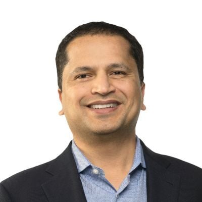 A smiling light-skinned male of Asian heritage with short black hair wearing a dark suit jacket over a light blue button-up shirt against a white backdrop
