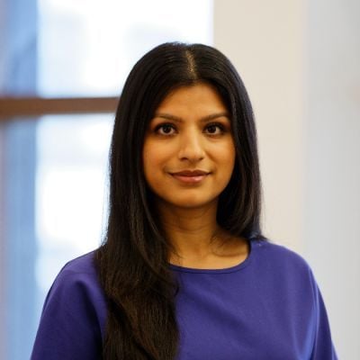 A smiling female of Asian heritage with long black hair wearing a blue shirt against a blurred background