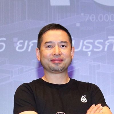 A lighter-skinned male with black hair wearing a black t-shirt with his arms crossed against an ambiguous background