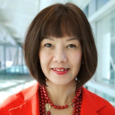 A smiling female of Asian heritage with short dark brown hair wearing a red jacket against a blurred background