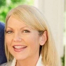 A smiling light-skinned female with blonde hair against an outdoor background