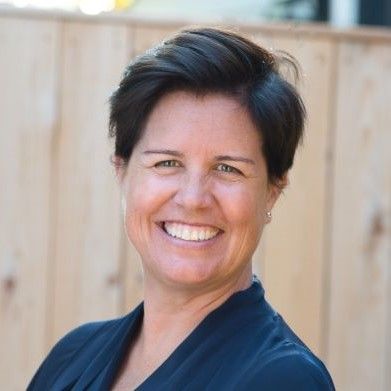 A smiling light-skinned female with short brown hair wearing a navy shirt against an ambiguous background