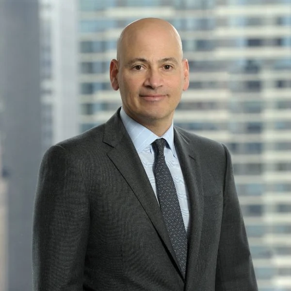 A smiling light-skinned male wearing a dark gray suit and tie against an ambiguous background