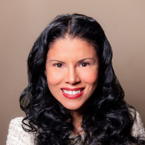 A smiling light-skinned female with long black hair wearing a white suit jacket against a tan background