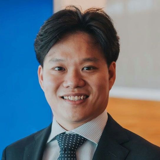 A smiling male of Asian heritage with black hair wearing a suit and tie against an ambiguous background