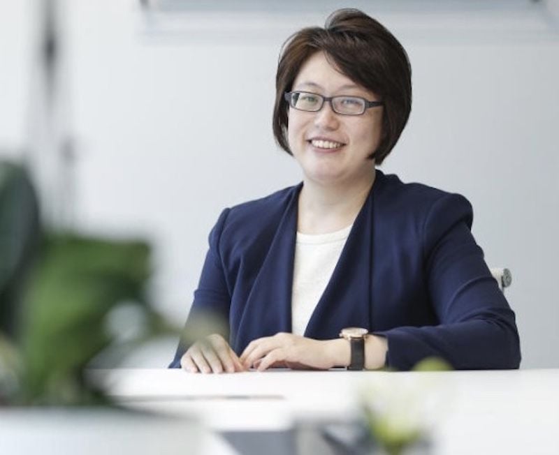 A smiling woman in an office wearing a navy blazer.