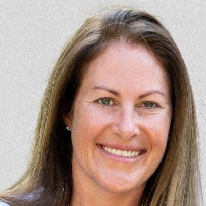 A smiling light-skinned female with long light brown hair against a light gray background