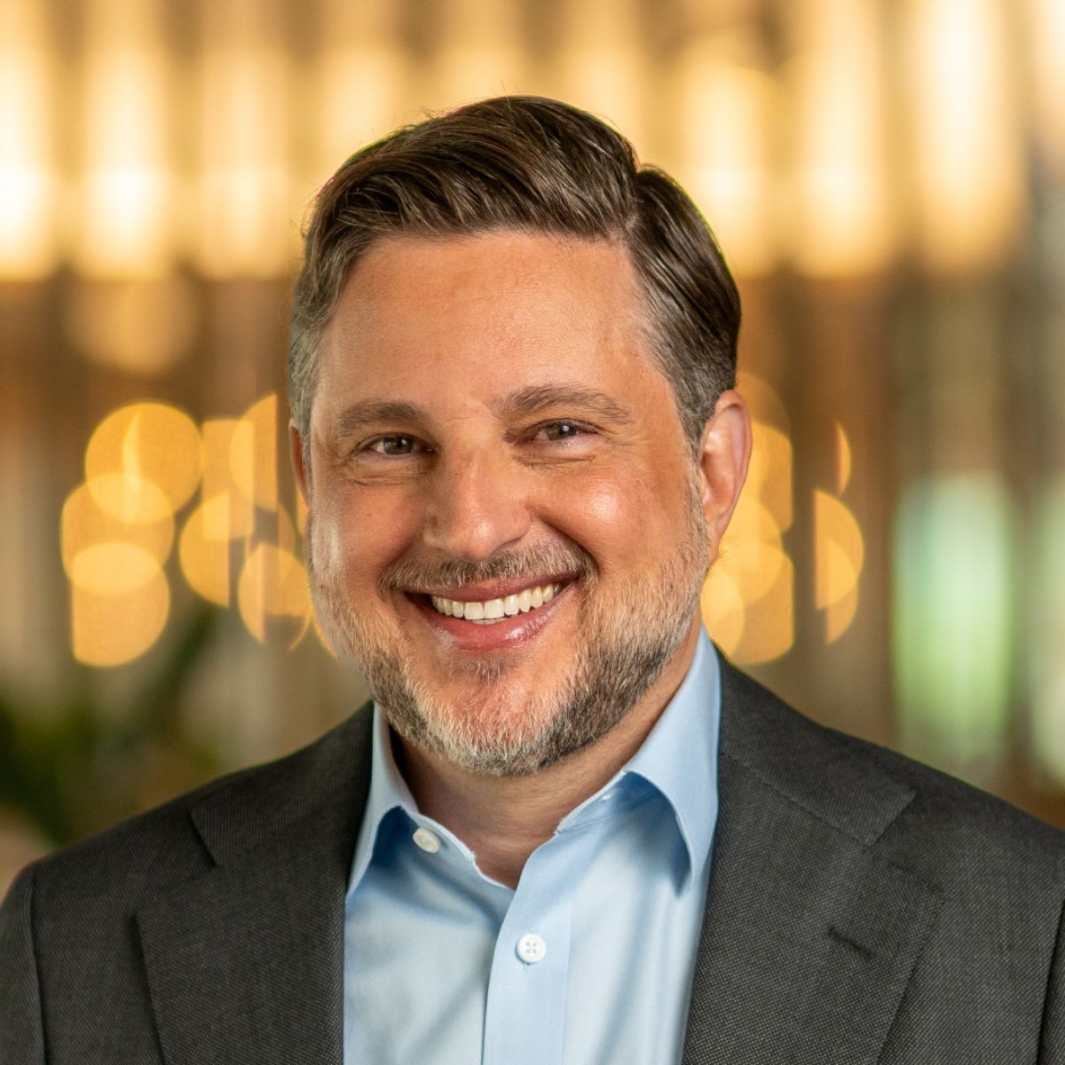 A headshot of a man named Peter Mintzberg who is a Fintech Advisory member of the Milken Institute. He is smiling and has a slight beard and short brown/gray hair, white skin, and is wearing a suit.