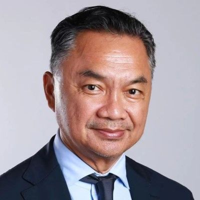 Dino Patti Djalal smiling slightly in a dark suit and light blue shirt, with a gray background.