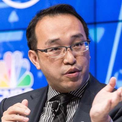 Kevin Lu gesturing while speaking, wearing glasses and a striped tie, seated in front of a CNBC panel backdrop.