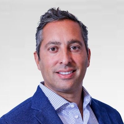 An image of Brett Tejpaul, who serves as Head of Coinbase Institutional. He is slightly smiling against a white background, wearing a blue suit with, and has gray hair.