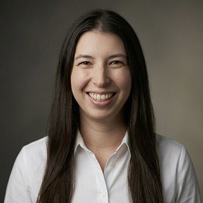 Professional headshot of smiling woman with long dark hair wearing white collared shirt