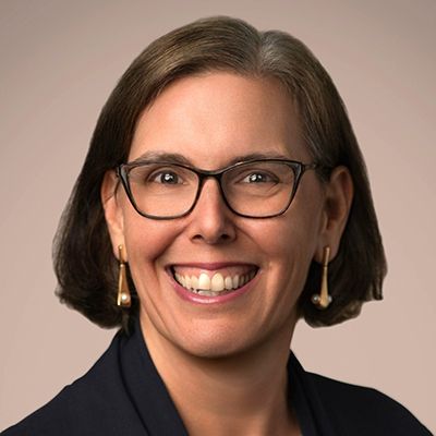 Professional headshot of a smiling woman with glasses and shoulder-length dark hair