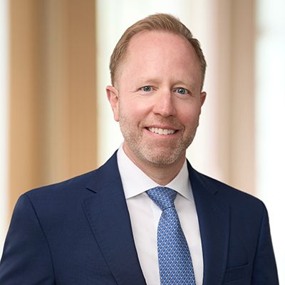 Professional headshot of smiling man in navy suit with blue patterned tie