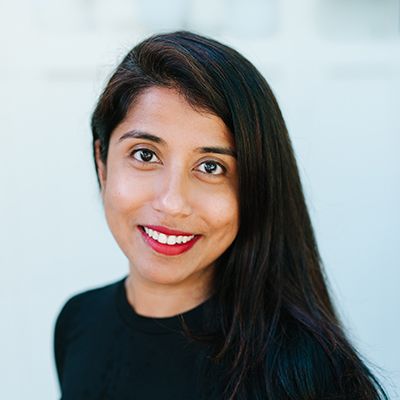 Professional headshot of woman with long dark hair and red lipstick smiling at camera