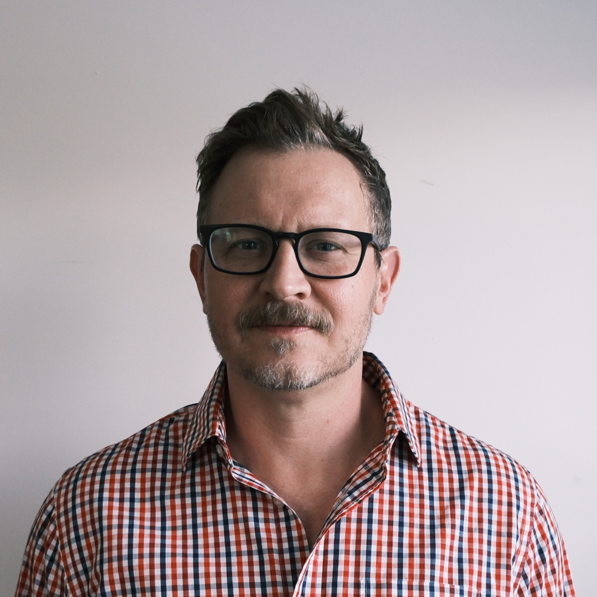 Man with glasses and mustache wearing checkered shirt against white background