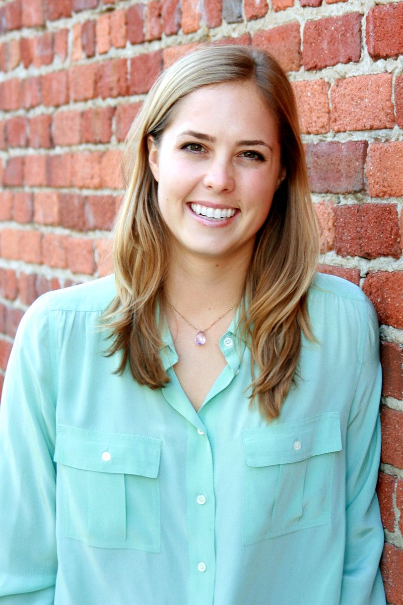 Woman smiling in mint green shirt against red brick wall