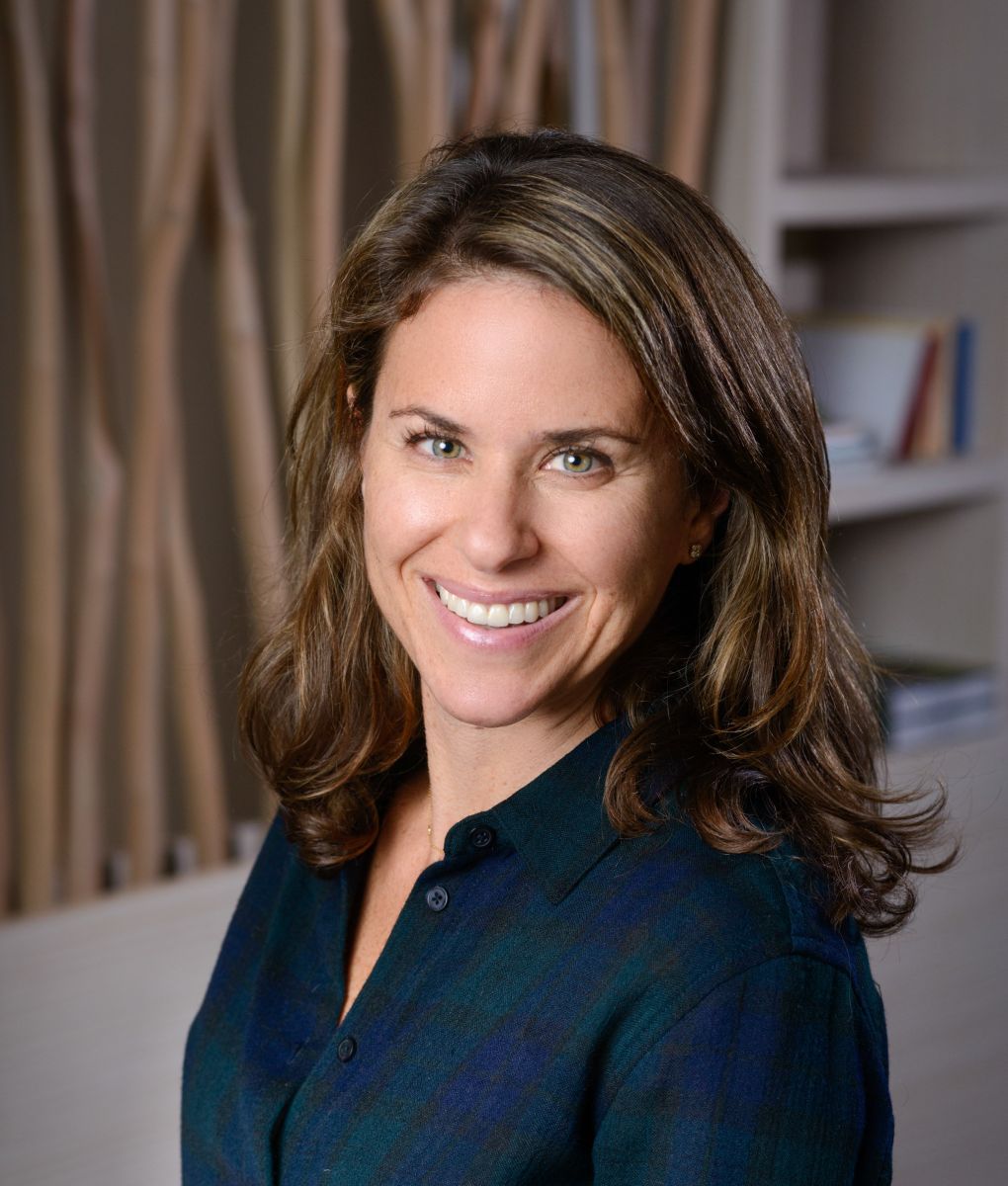 Professional headshot of a smiling woman with brown hair wearing a dark blue top