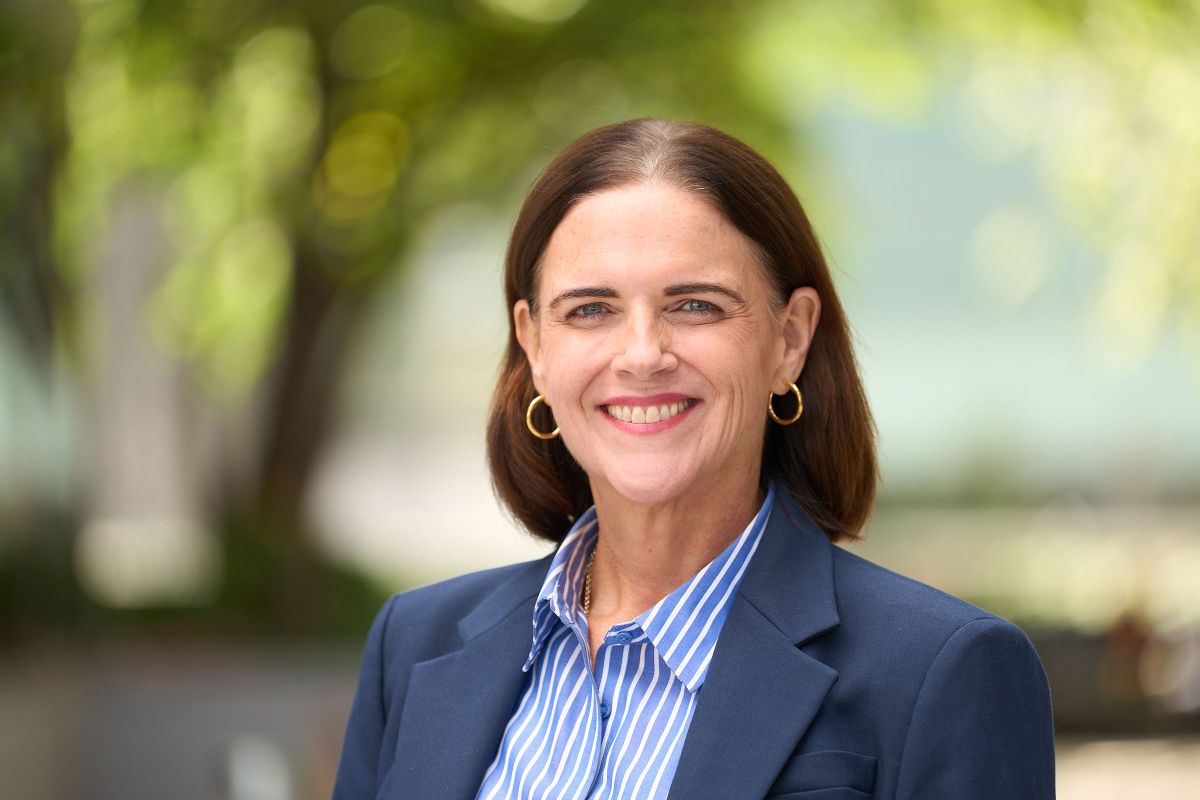 Professional headshot of a smiling woman in a navy blazer and striped shirt outdoors