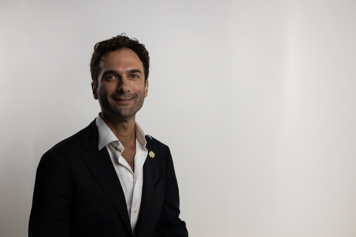 Man with beard smiling in black blazer and white shirt against white wall