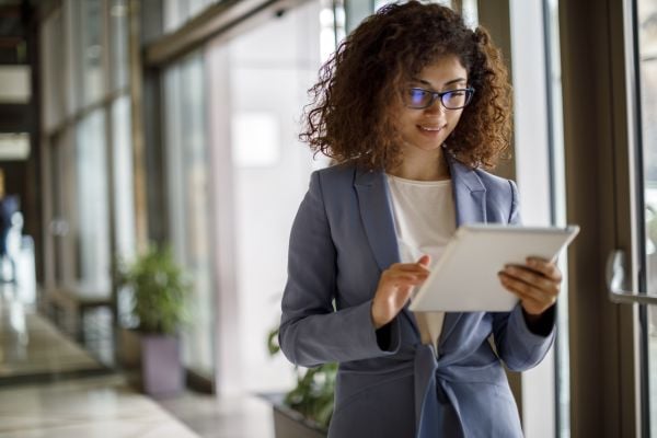 Female-presenting individual with darker skin and brown curly hair wearing a blue suit stands with papers in her hand in an office setting