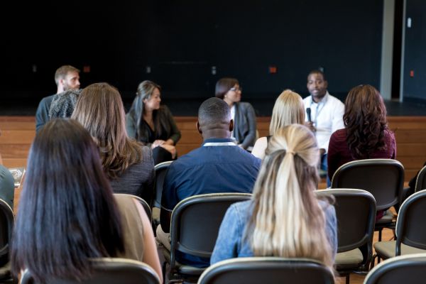 A group of people sit looking forward to watch a panel of speakers talk