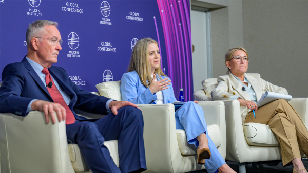 An image of three adults sitting in white chairs on a stage at the Milken Institute Global Conference 2025. To the left is a man who is older in appearance with short gray hair, white skin, and wearing glasses and a navy blue suit with a red tie. In the middle is a woman with long blonde hair and white skin who is wearing a light blue suit. To the right is a person with short blonde hair and white skin wearing a light colored suit.