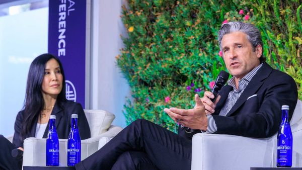Lisa Ling (left, she has long black hair, white skin, and is wearing a black blazer) talking to Patrick Dempsey (right, he has gray and white hair, white skin, and is wearing a dark suit while actively speaking and holding a microphone) at the 28th Milken Institute Global Conference in Los Angeles, California.